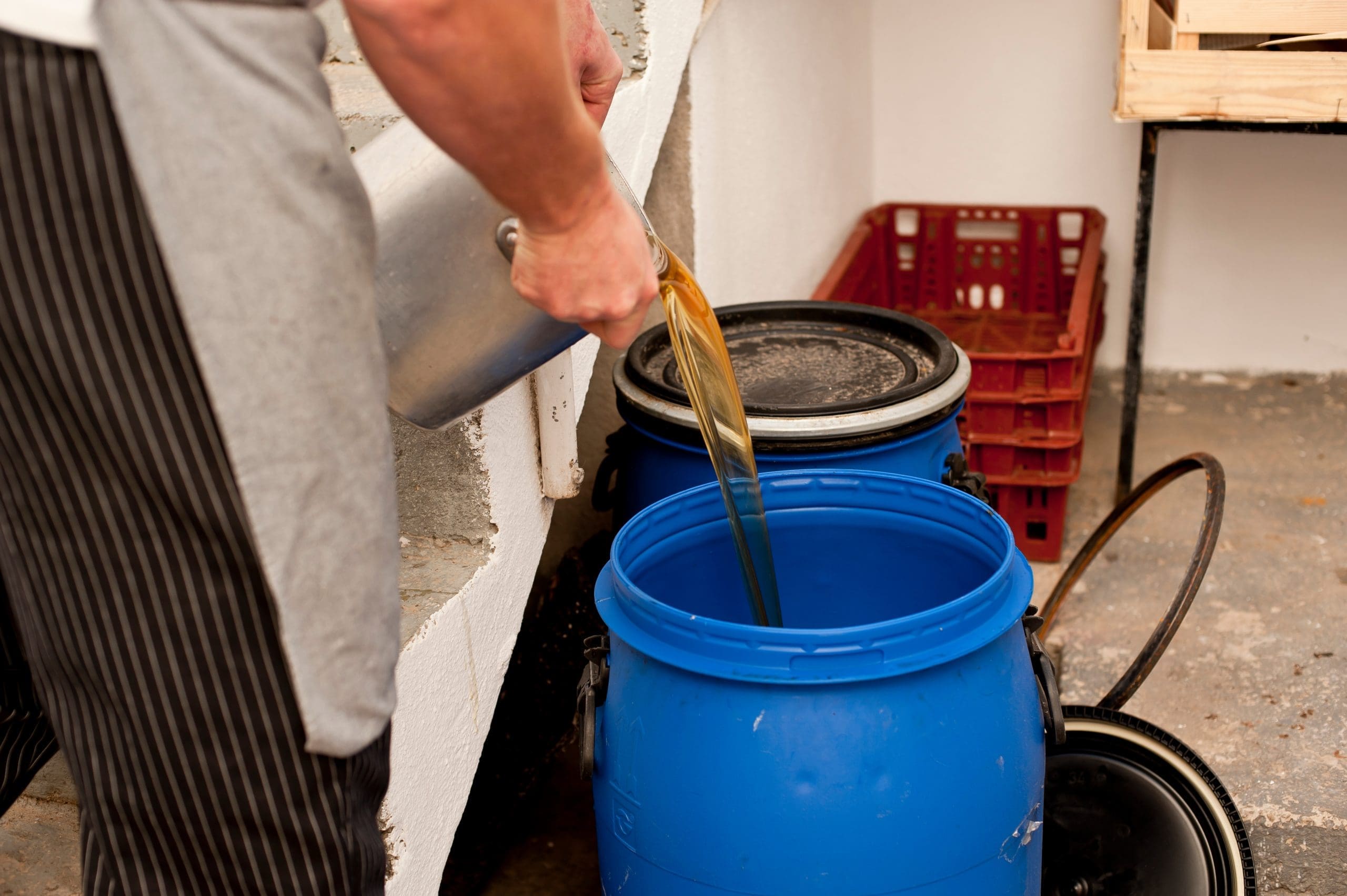Used cooking oil being poured into a blue plastic open top drum for collection and recycling